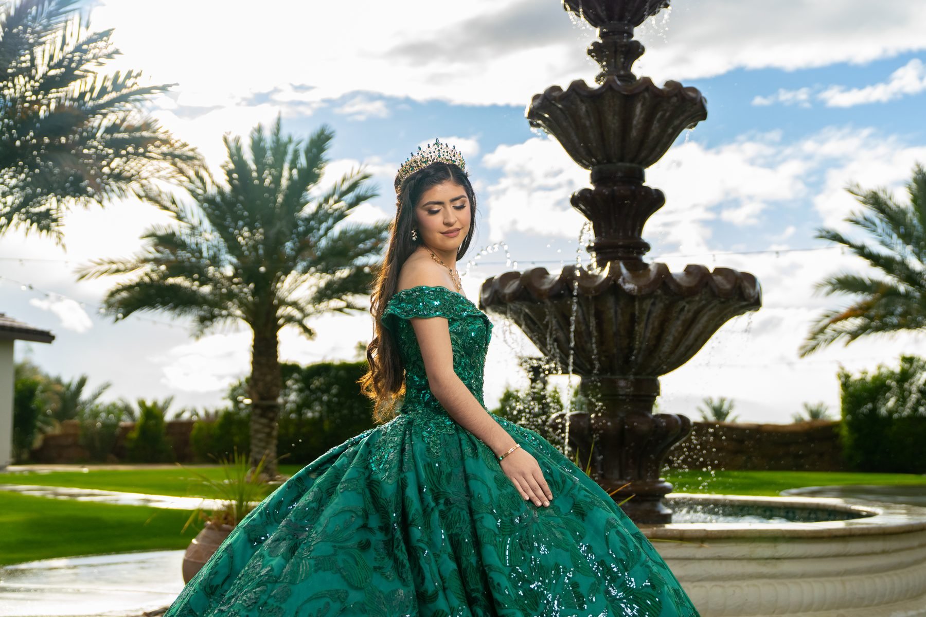 Quinceañera twirling in emerald ball gown beside the fountain and palms at Rancho Escondido in Indio.