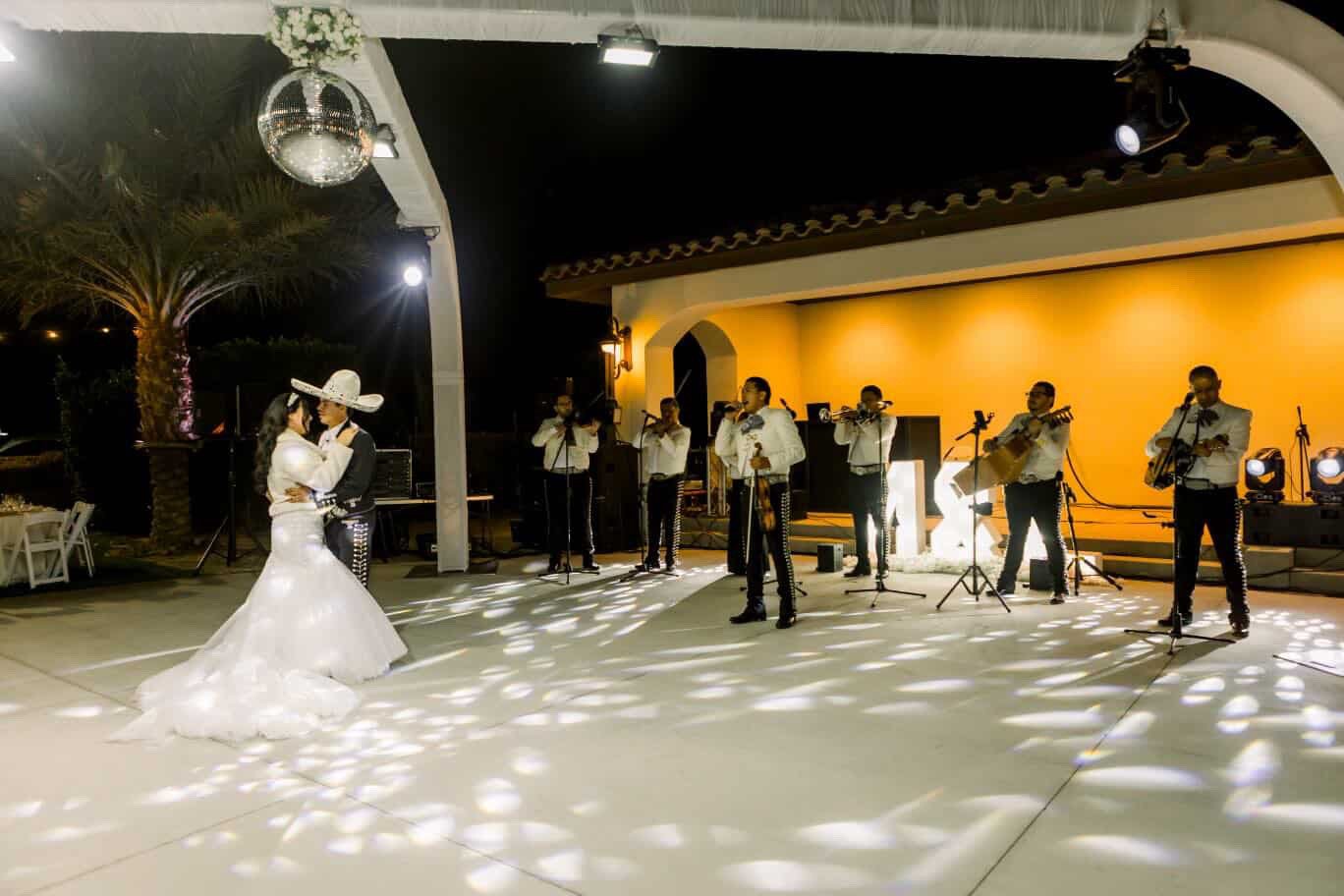 Bride and groom dancing while mariachi band plays under the lit pergola at Rancho Escondido wedding.