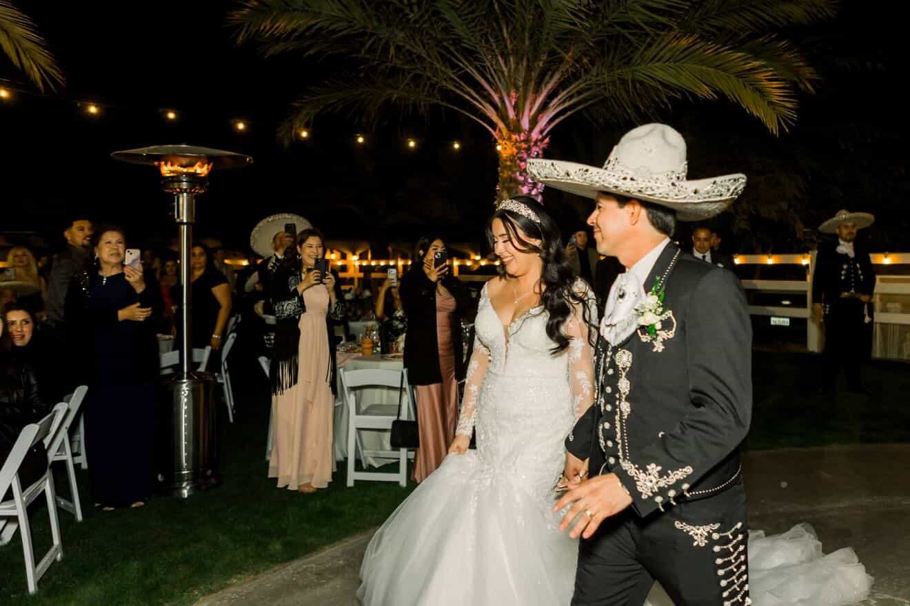 Bride and groom grand entrance walking past palm trees and string lights at Rancho Escondido wedding.